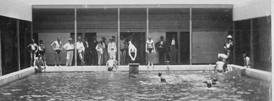 Old black and white image of Coolgardie Swimming Pool with people standing along the edge and some in the water