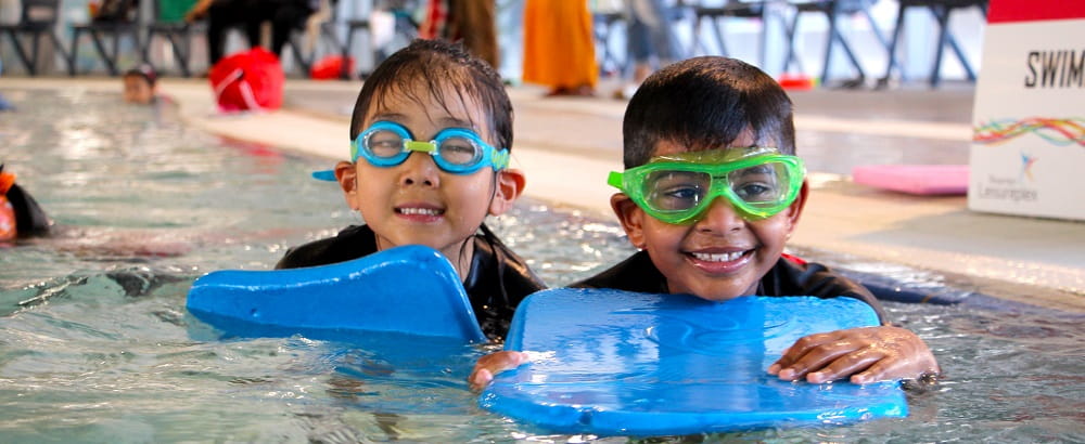 children in a public swimming pool wearing goggles and smiling