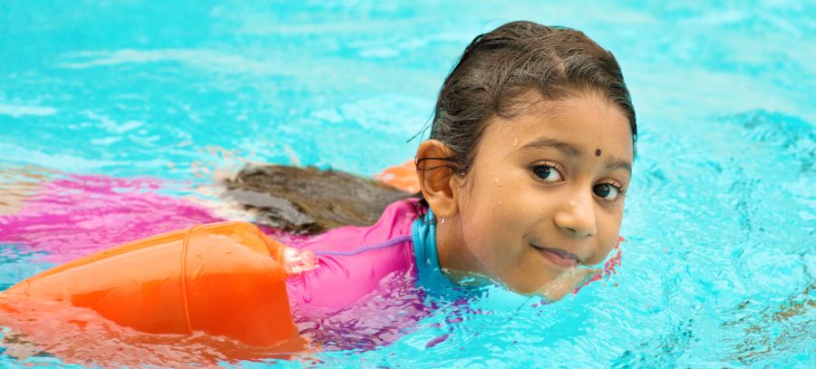 A little girl swimming in a pool wearing floaties