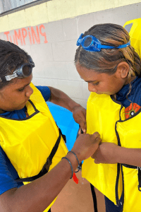 Two kids help one another with their lifejackets