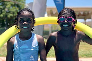two Aboriginal children with a pool noodle smiling at camera