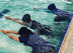 Three multicultural women in the pool with faces in the water as part of their swimming lesson