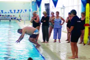 A man diving into the pool with others watching on