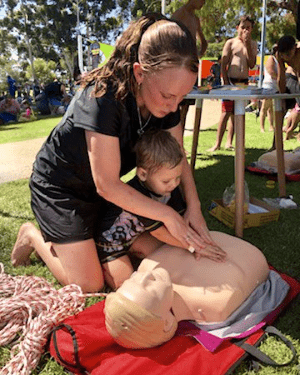 A mum with a toddler practising CPR on a manikin