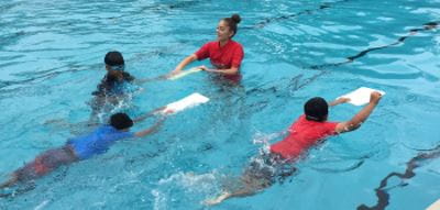 An instructor in the water with three boys swimming with kickboards
