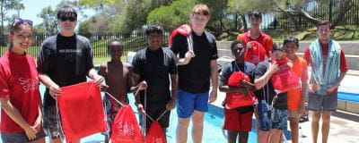 Swim instructors and students by the pool with their Swim and Survive bags
