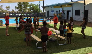 Aboriginal children standing on the grass by the pool learning skills from their two instructors