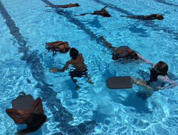 Aboriginal children floating on their back in the pool holding kickboards