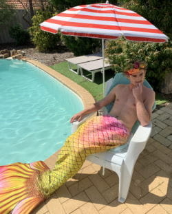 A young man dressed as a mermaid sitting on a chair by a pool
