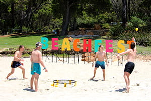 Teenagers on the beach playing games in front of a Beachfest sign