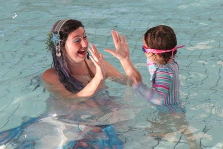 Woman dressed as mermaid giving high fives to child