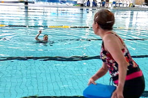 A woman throwing a kickboard to a man in the pool