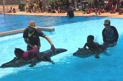 Two aboriginal children on inflatable crocodiles beaing led by their teaches across the pool in Bidyadanga