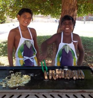 Two aboriginal boys cooking sausages and onions on a BBQ