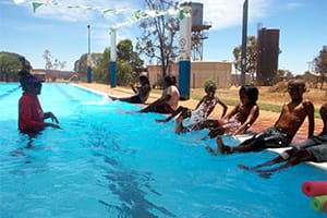 Children sitting along the edge of the pool with their instructor in the water