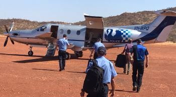 Police walking to a police plane amongst red dirt