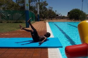 An Aboriginal boy sliding on his back on a Slip N Slide by the pool