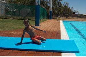 An Aboriginal boy on a blue Slip N Slide by the pool