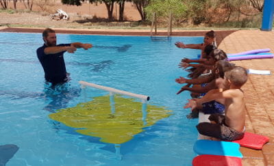 Instructor Aaron Jacobs in the pool with aboriginal children along the edge during their swimming lessons