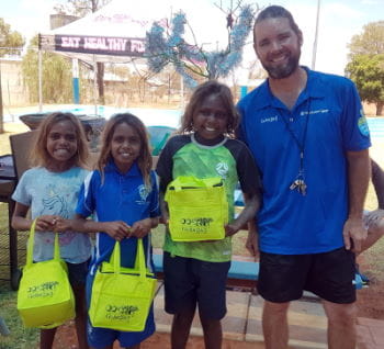 Pool Manager Aaron Jacobs with three aboriginal children holding Swim for Fruit prize bags