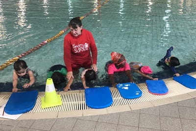 multicultural children using kickboards at a swimming lesson