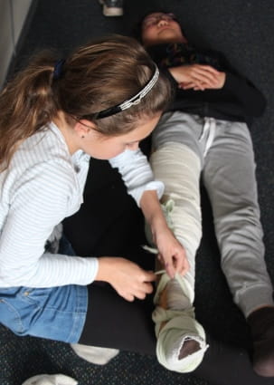 image of young girl bandaging another girl's leg