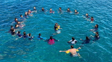 A group of students in a ciircle in the ocean with their teachers
