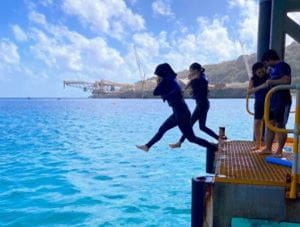 Two girls jumping off a jetty into the ocean