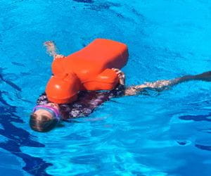 A young girl swimming on her back pulling an orange lifesaving manikin