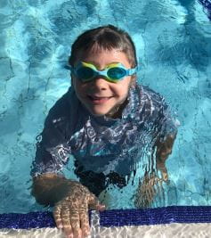 A young boy wearing goggles enjoying his swimming lesson at Collie