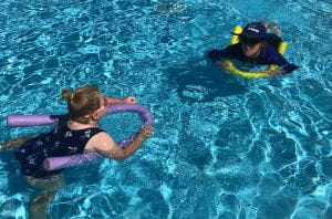 A young girl with a pool noodle swimming to her instructor in Collie
