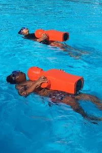 Two children swimming on thier back with orange lifesaving manikins