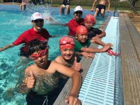 Two swim instructors in the water with multicultural children at Lynwood Senior High School