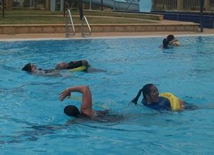 Two pool managers swimming each with another person being towed behind in a rescue tube