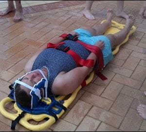 image of a patient strapped to a spinal board by the side of a pool
