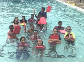 A group of multicultural children in the pool holding kickboards