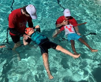 Two swim instructors with two children learning to float on their backs