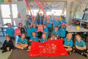 A group of children sitting in a classroom with a Swim and Survive banner