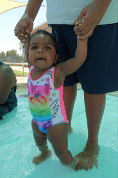 Aboriginal baby girl standing in swimming pool with her mother