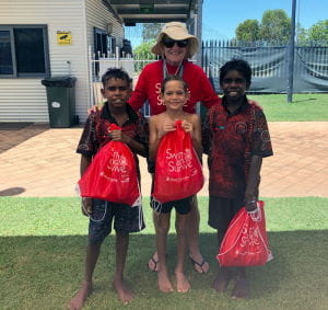 Swim Instructor Susan Reeve with three aboriginal boys at Fitzroy Crossing holding Swim and Survive bags