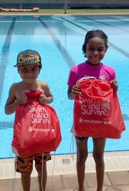 two young Aboriginal children holding Swim and Survive packs in front of a pool