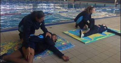Two students from Geraldton Girls Academy leaning over other students practising first aid skills