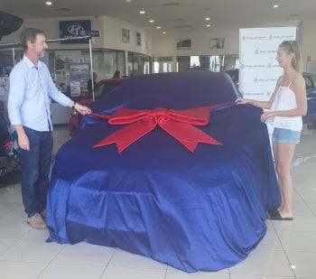 Raffle winner Dean English and daughter Carrie with their car under a blue cover with a red bow