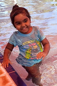 A toddler girl smiling as she plays in the pool