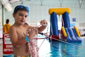 A young boy with a rescue rope by the pool with an inflatable in the background