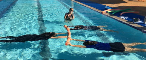 Women floating face down in the pool holding a pool noodle