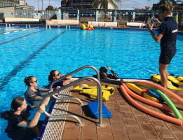 Four trainees in the water listening to their trainer standing by the pool