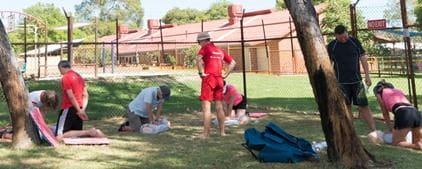 A group of people practising CPR skills on the grassed area by the pool at Hollywood Primary