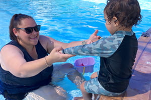 Aboriginal mum and toddler son practice arm's reach in the pool