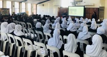 Girls wearing white Islamic headdresses sitting watching a water safety presentation